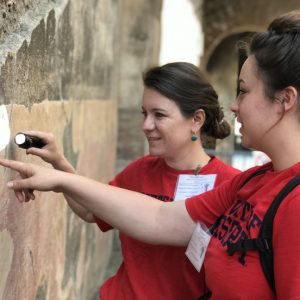 acqueline DiBiasie-Sammons (left) and Ole Miss student Anne Acevedo search a wall for traces of ancient graffiti using a flashlight during a trip to Pompeii in 2019. The professor’s presentation of 'A Day in Ancient Pompeii' was selected by TED for global broadcast. Submitted photo